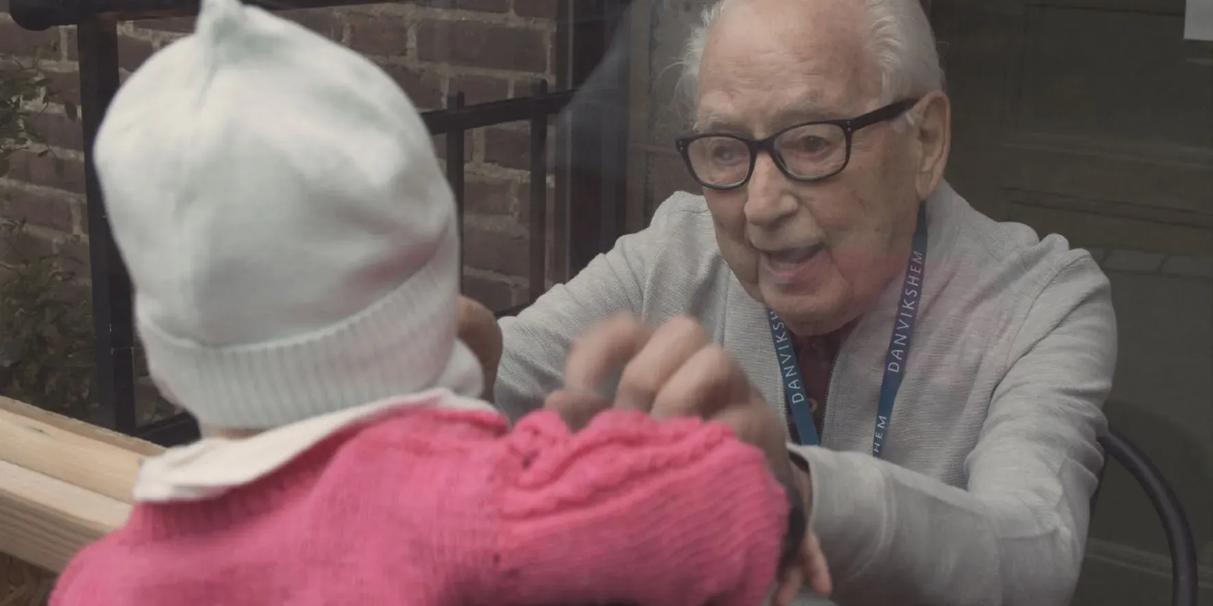 An elderly man reaching out to a small child in a knitted hat